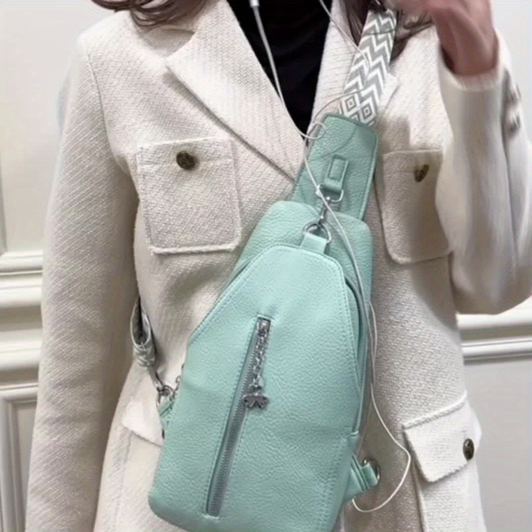 Donna con cappotto bianco indossa borsa a tracolla verde menta in pelle, con cerniera e tracolla decorata. Accessorio moda elegante e pratico.