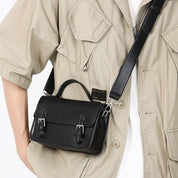 Borsa a tracolla nera in pelle con fibbie, indossata su camicia beige. Accessorio moda elegante e versatile per uomo e donna.