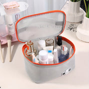 Borsa organizer cosmetici trasparente con cerniera arancione, contenente flaconi di creme e lozioni, su tavolo da trucco. Accessorio viaggio pratico.