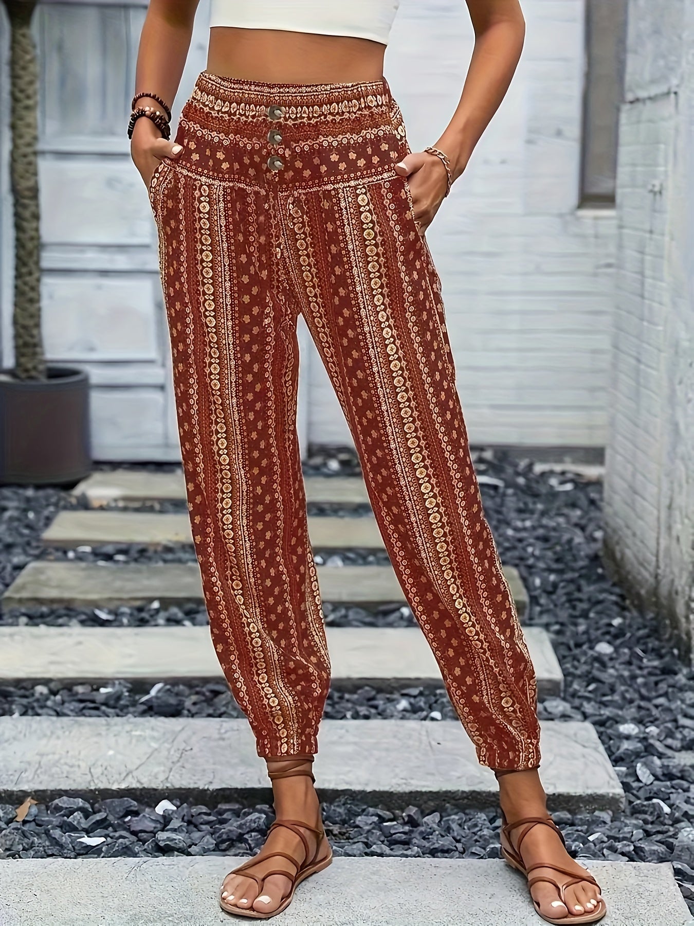 Pantaloni boho a vita alta con stampa etnica rossa, tasche laterali, indossati da una donna con sandali marroni. Moda estiva casual.