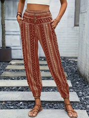 Pantaloni boho a vita alta con stampa etnica rossa, tasche laterali, indossati da una donna con sandali marroni. Moda estiva casual.
