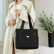 Donna con cappotto beige e borsa a tracolla nera elegante. Accessorio moda femminile, borsa capiente, design moderno. Sfondo interno con pianta.