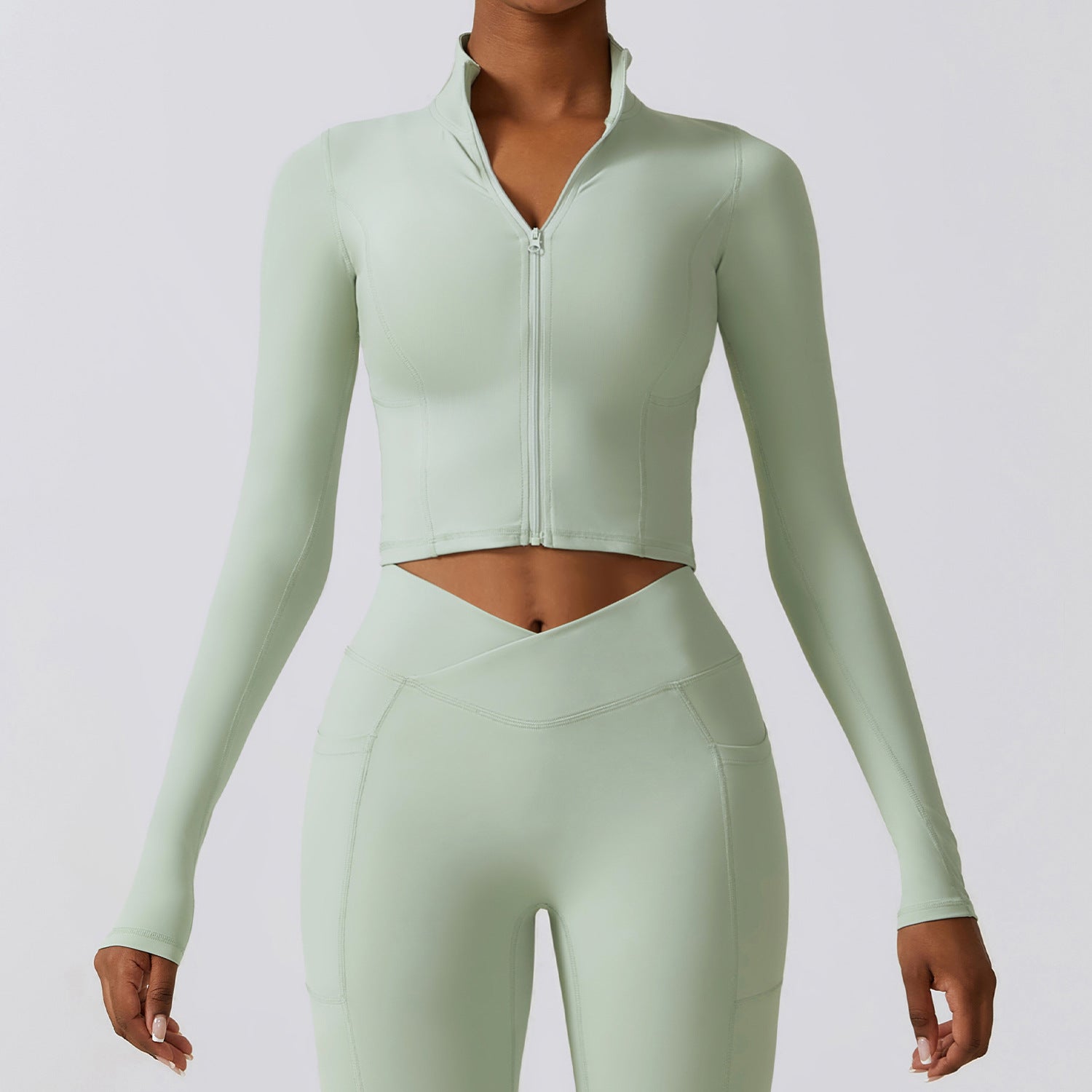 Giacca sportiva donna verde menta, maniche lunghe, zip frontale, abbinata a leggings a vita alta. Abbigliamento fitness elegante e moderno.