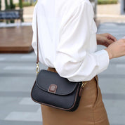 Donna con borsa a tracolla in pelle nera, elegante e moderna, indossa camicia bianca e gonna marrone. Accessorio moda femminile di tendenza.