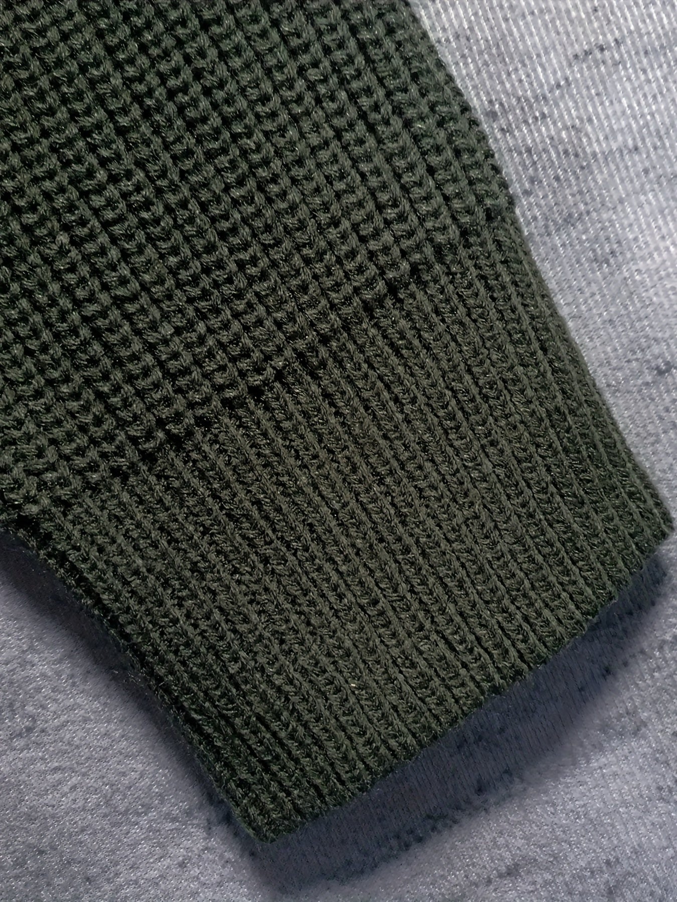 Manica maglione verde scuro in maglia a coste su sfondo grigio. Tessuto caldo e morbido, ideale per l'inverno. Moda uomo, abbigliamento casual.