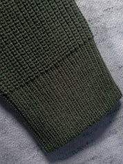 Manica maglione verde scuro in maglia a coste su sfondo grigio. Tessuto caldo e morbido, ideale per l'inverno. Moda uomo, abbigliamento casual.