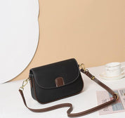 Borsa a tracolla in pelle nera con dettagli marroni su sfondo beige, elegante e versatile, perfetta per moda donna. Accessorio chic e funzionale.