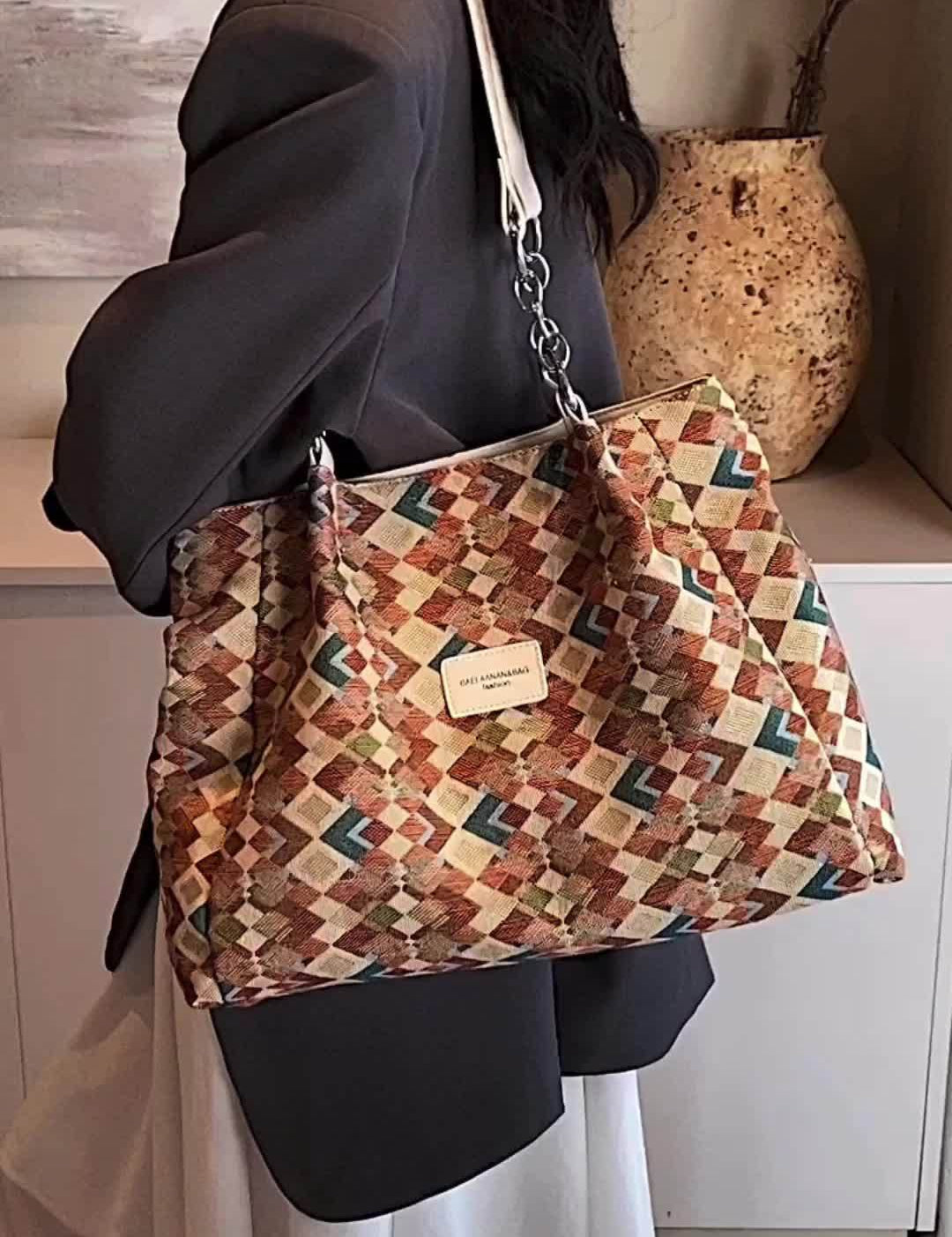 Borsa a tracolla multicolore con motivo geometrico, indossata da una persona in giacca grigia. Accessorio moda elegante e versatile.