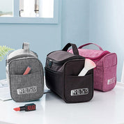 Tre borse da toilette in tessuto grigio, nero e rosa su un tavolo, con cerniere e tasche esterne, ideali per organizzare cosmetici e accessori da viaggio.