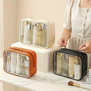Borse da toilette trasparenti in tre colori (bianco, marrone, nero) su tavolo, contenenti flaconi cosmetici. Ideali per viaggi, organizzazione trucco.