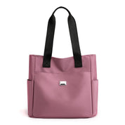 Borsa tote rosa in tessuto con manici neri, tasche laterali e logo frontale. Elegante e pratica per uso quotidiano. Accessorio moda donna.