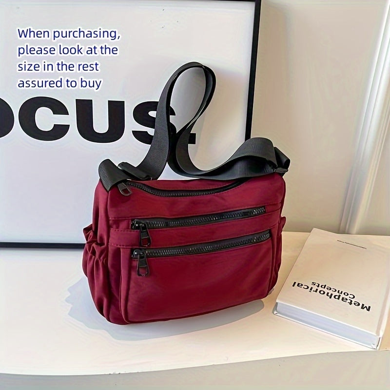 Borsa a tracolla rossa con cerniere multiple su sfondo bianco, accanto a un libro. Design elegante e pratico per moda femminile.