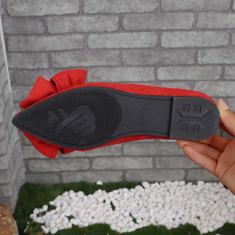 Scarpa da donna rossa con suola in gomma nera, design a punta, sfondo in mattoni grigi e ciottoli bianchi. Scarpe eleganti, moda femminile.
