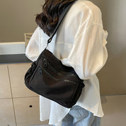Donna con camicia bianca indossa borsa a tracolla nera con tasche multiple, stile casual. Accessorio moda femminile, pratico e versatile.
