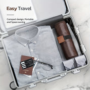 Valigia aperta con camicia grigia, custodia in pelle, passaporto e occhiali. Design compatto, ideale per viaggi facili e salvaspazio.
