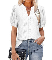 Blusa bianca traforata da donna con maniche a sbuffo, scollo a V, abbinata a jeans blu e borsa nera. Moda estiva casual elegante.