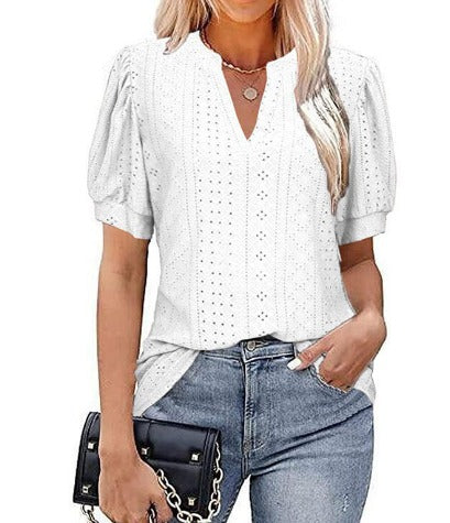 Blusa bianca traforata da donna con maniche a sbuffo, scollo a V, abbinata a jeans blu e borsa nera. Moda estiva casual elegante.