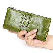 Portafoglio in pelle verde lucida tenuto in mano, con chiusura a bottone e cerniera. Accessorio moda elegante e pratico per donna.