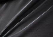 Tessuto in ecopelle nera, superficie liscia e lucida, ideale per abbigliamento e arredamento. Materiale resistente e di alta qualità.