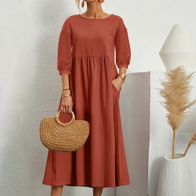 Abito lungo rosso terracotta con maniche a tre quarti, borsa in paglia intrecciata, sfondo bianco minimalista, moda donna elegante.