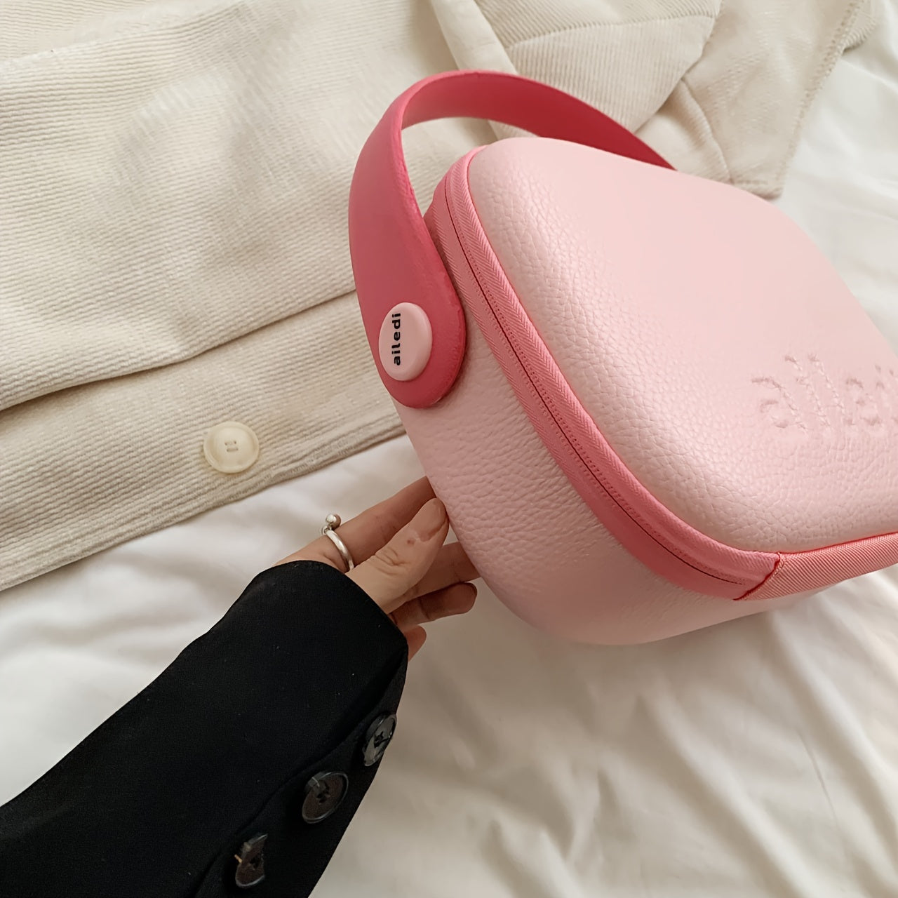 Borsa a tracolla rosa in pelle con logo in rilievo, manico rosso, su sfondo di tessuto beige. Accessorio moda elegante e moderno.