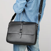 Borsa a tracolla in pelle nera, indossata su camicia di jeans. Design elegante, ideale per lavoro e viaggio. Accessorio moda uomo.