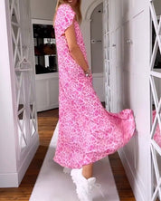 Donna con abito lungo rosa leopardato, scarpe da ginnastica bianche, in un corridoio elegante. Moda femminile, abbigliamento casual chic.