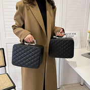 Donna con cappotto beige tiene due borse nere trapuntate con manico in metallo, design elegante e moderno, accessori moda femminile.