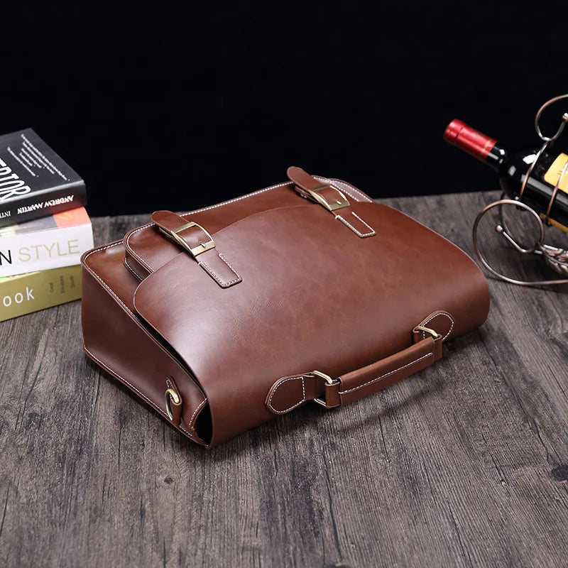 Borsa a tracolla in pelle marrone su tavolo di legno, con fibbie dorate. Elegante accessorio moda uomo, ideale per lavoro e viaggi.