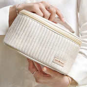 Borsa cosmetica rotonda beige con cuciture a righe, manico superiore e chiusura lampo. Ideale per viaggi, organizzazione trucco e accessori.