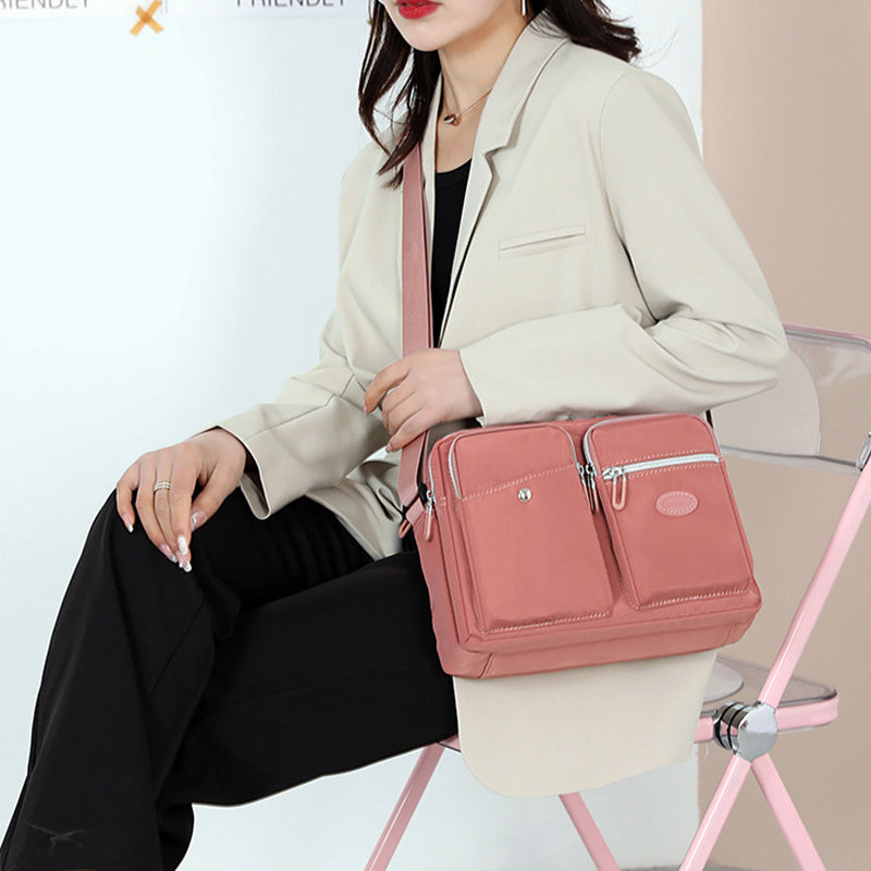 Donna con borsa a tracolla rosa, giacca beige e pantaloni neri, seduta su sedia trasparente. Accessorio moda femminile elegante e pratico.