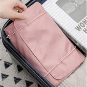 Utente che inserisce un organizer da viaggio rosa in una valigia aperta, accanto a una rivista. Accessorio pratico per organizzare bagagli.