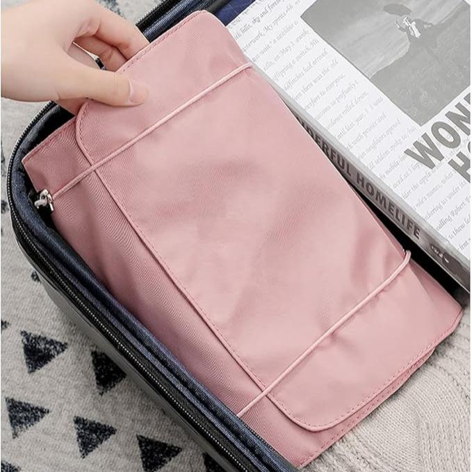 Utente che inserisce un organizer da viaggio rosa in una valigia aperta, accanto a una rivista. Accessorio pratico per organizzare bagagli.