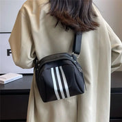 Borsa a tracolla nera con strisce bianche, indossata su cappotto beige. Design moderno, ideale per moda casual e urbana. Accessorio unisex.