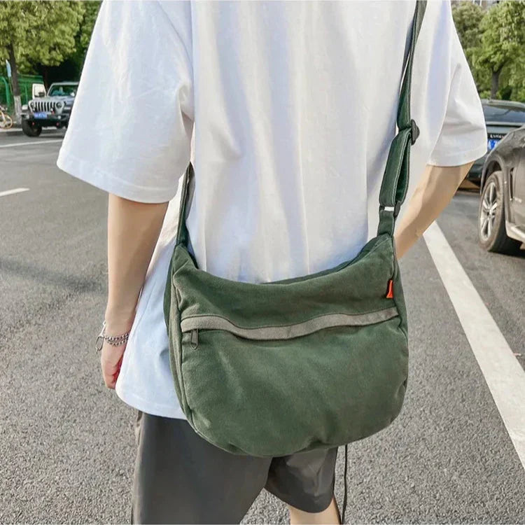 Uomo con borsa a tracolla verde in tessuto, indossa maglietta bianca e pantaloncini neri, in strada cittadina. Accessorio moda casual unisex.