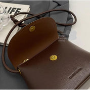 Borsa a tracolla in pelle marrone con chiusura magnetica, design elegante, su sfondo grigio. Accessorio moda donna, stile casual chic.