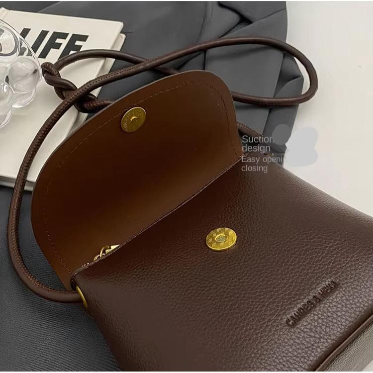 Borsa a tracolla in pelle marrone con chiusura magnetica, design elegante, su sfondo grigio. Accessorio moda donna, stile casual chic.