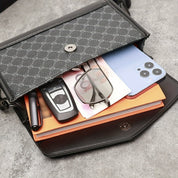 Borsa a tracolla in pelle nera con portafoglio, occhiali, smartphone, chiavi auto e penna su sfondo grigio. Accessori eleganti e funzionali.