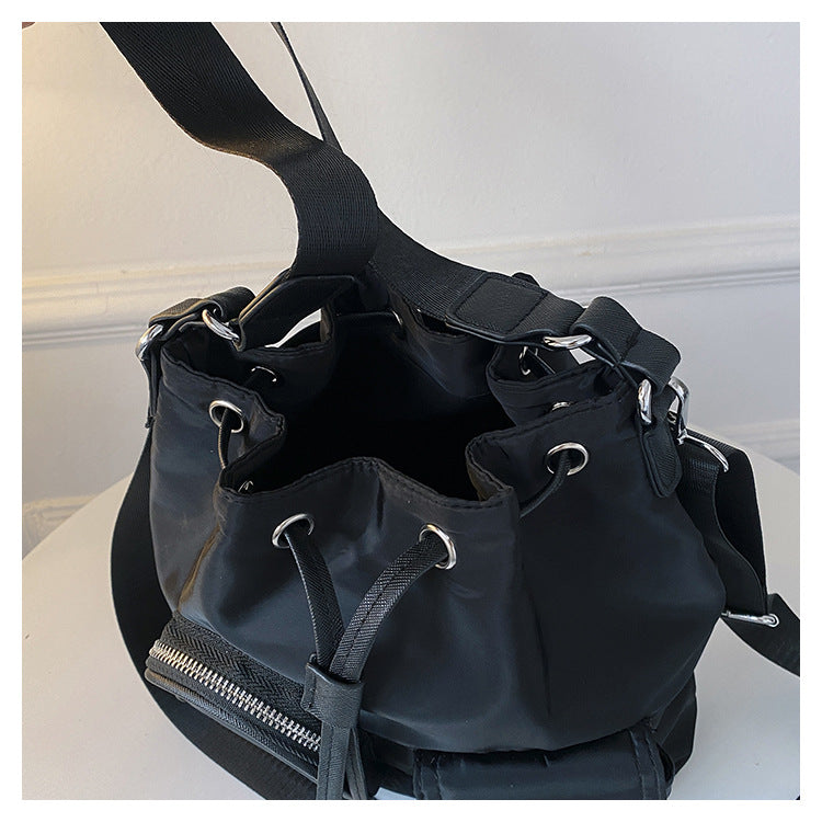 Zaino nero in nylon con chiusura a coulisse, dettagli in metallo argentato e cerniera frontale. Design moderno e spazioso, ideale per l'uso quotidiano.