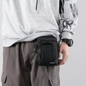 Borsa a tracolla nera da uomo, compatta e funzionale, indossata su pantaloni cargo grigi. Ideale per viaggi, escursioni e uso quotidiano.