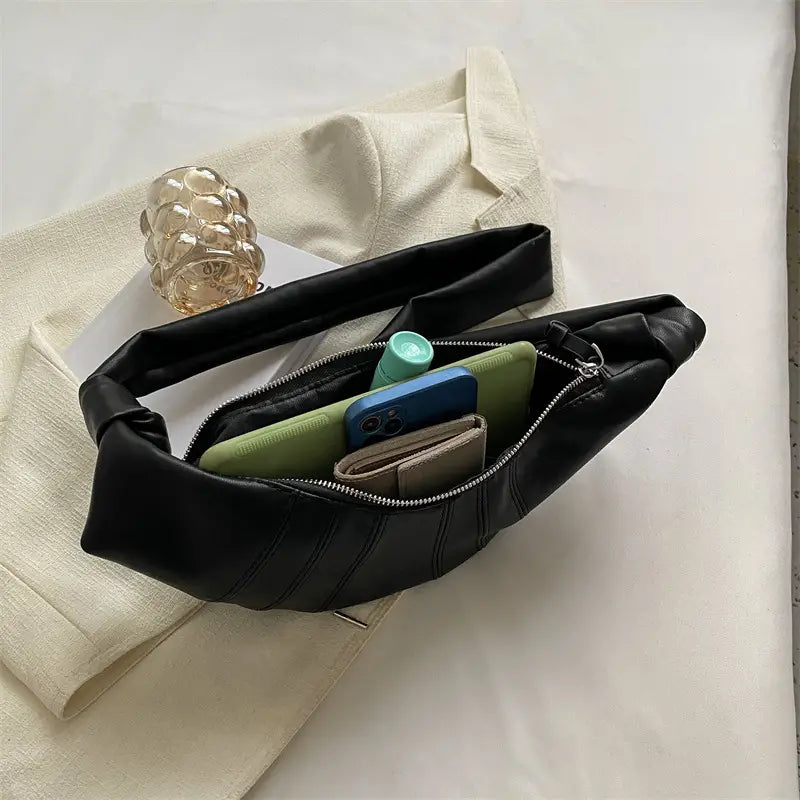 Marsupio nero in pelle su tessuto beige, aperto con smartphone, portafoglio e accessori visibili. Design elegante, moda accessori donna.