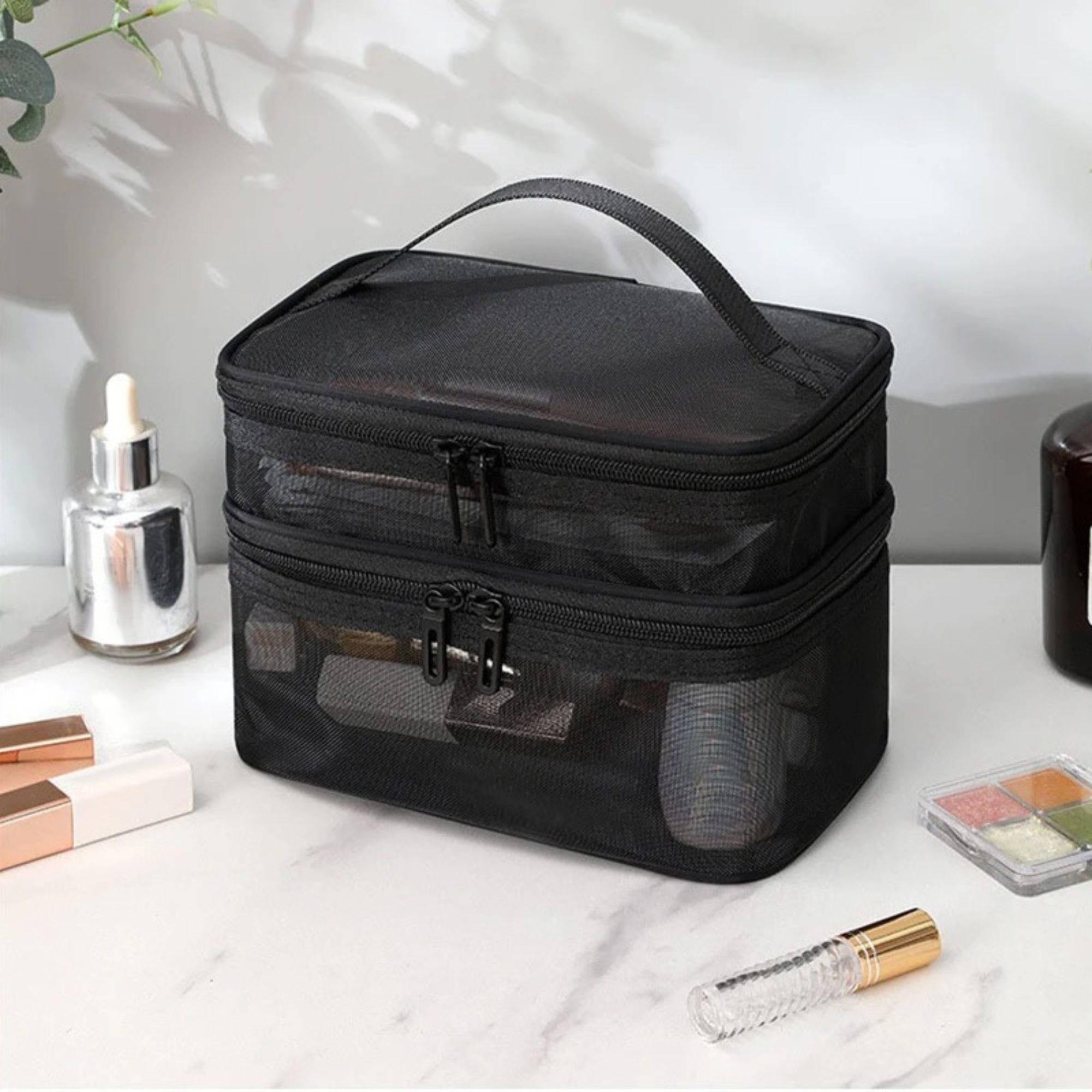 Borsa trucco nera a due scomparti con cerniera, manico superiore, su tavolo bianco. Include flaconi cosmetici e palette ombretti. Accessori bellezza.