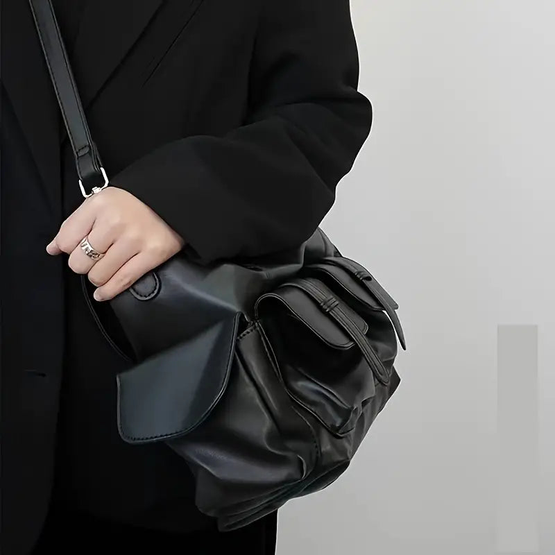 Borsa a tracolla in pelle nera, design elegante e moderno, indossata da una persona in abito scuro. Accessorio moda versatile e di tendenza.