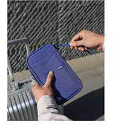 Persona che tiene un portafoglio da viaggio blu con cerniera, vicino a una valigia argentata. Accessorio organizzatore per documenti e passaporti.