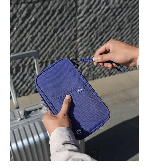 Persona che tiene un portafoglio da viaggio blu con cerniera, vicino a una valigia argentata. Accessorio organizzatore per documenti e passaporti.