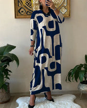Abito lungo donna a maniche lunghe con stampa geometrica blu e beige, stile casual chic, perfetto per moda autunnale. Arredamento moderno sullo sfondo.