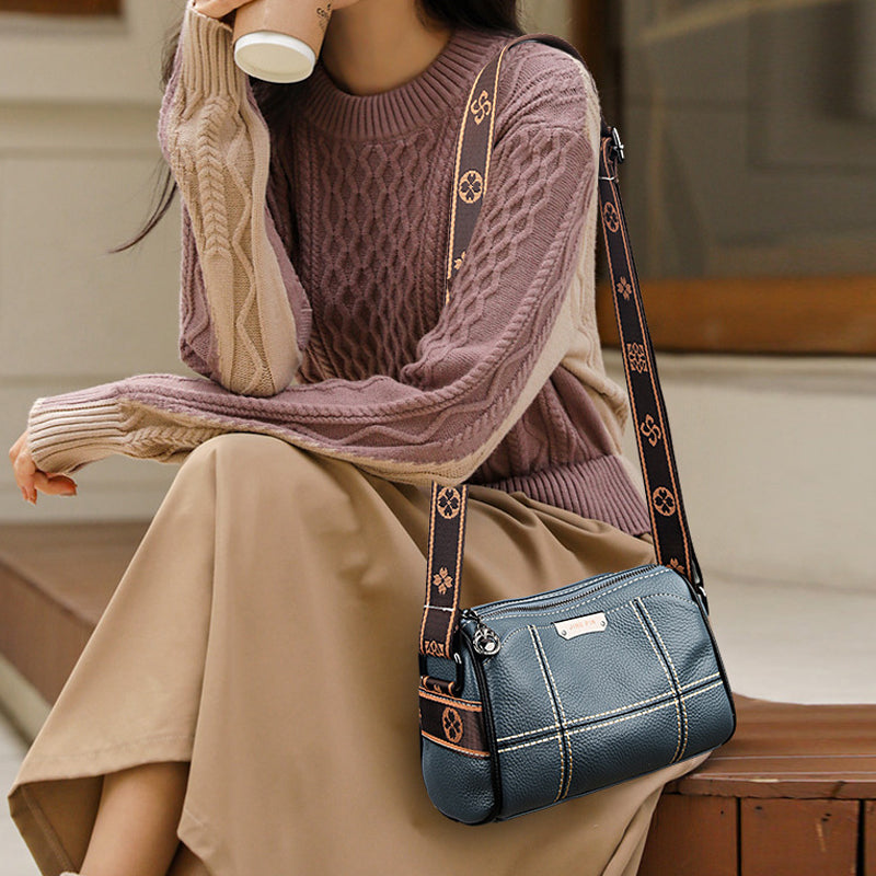 Donna con maglione intrecciato e borsa a tracolla blu in pelle, seduta su una panchina. Moda autunnale, accessori eleganti, stile casual chic.