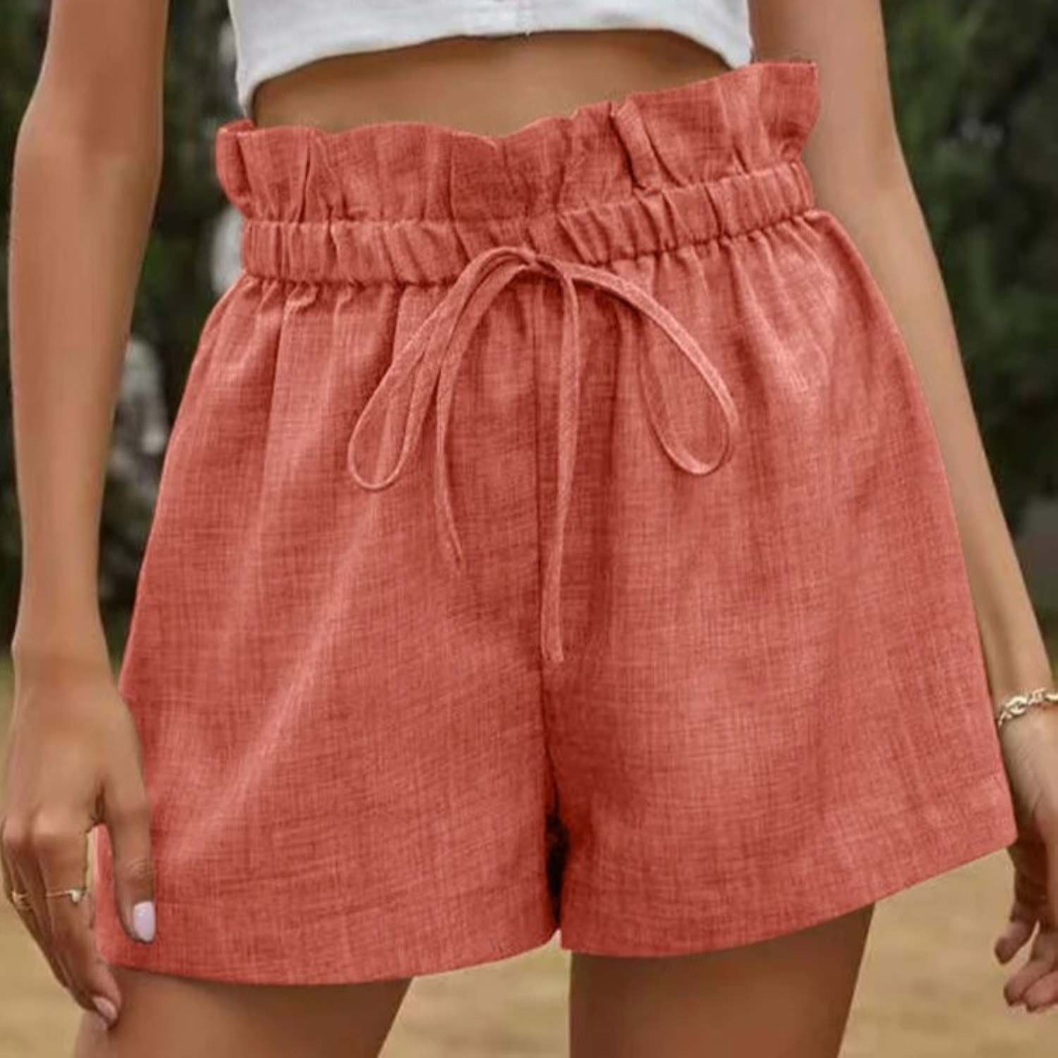 Shorts a vita alta in lino rosso arricciato con cintura a laccio, indossati da una donna. Stile estivo casual, moda femminile trendy.
