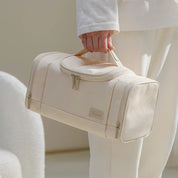 Borsone da viaggio beige in tessuto, con doppia cerniera e manico, tenuto da una persona. Design elegante e minimalista.