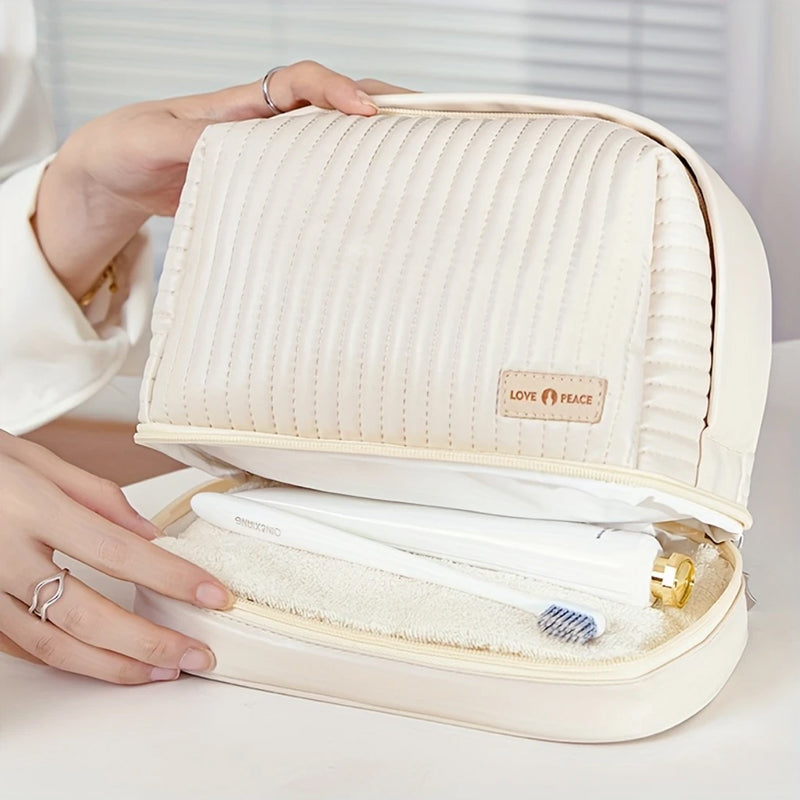 Borsa da toilette beige trapuntata con cerniera, contenente spazzolino e asciugamano. Design elegante, ideale per viaggi e organizzazione bagno.